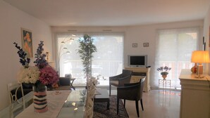 Una sala de estar moderna con una mesa de comedor de vidrio, un sofá, un televisor y un balcón con vistas.