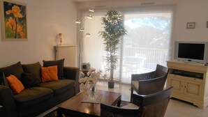 Una sala de estar con sofá, sillas, una mesita de centro, una planta en maceta y un televisor.