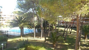 Zona de piscina rodeada de árboles y un edificio con balcones al fondo.