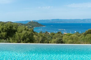 Blick auf einen Pool mit Meer- und Hügellandschaft im Hintergrund.