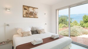 Une chambre dotée d’un grand lit, de draps blancs et offrant une vue sur un paysage naturel grâce à une porte-fenêtre coulissante.