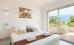 Ein Schlafzimmer mit einem großen Bett, weißen Leinen und Blick auf eine natürliche Landschaft durch eine Glastür.