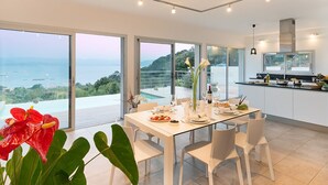 Un espace repas moderne avec une table en verre, des chaises blanches et une vue sur la mer.