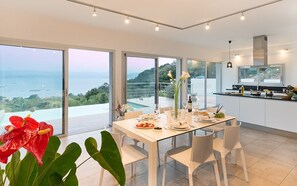 Ein moderner Essbereich mit einem Glastisch, weißen Stühlen und Meerblick.