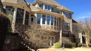 A two-story house with a stone foundation, large windows, and a gabled roof.