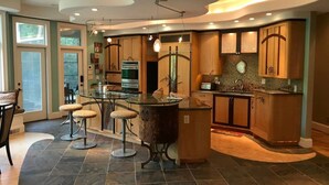 A modern kitchen with a curved island, bar stools, and a dining area with a glass table.