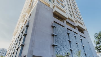 A tall, modern building with a unique facade featuring perforated panels and a large entrance.