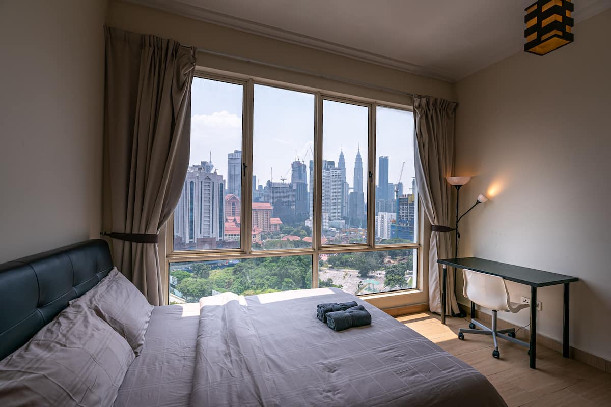 A bedroom with a large window, a bed, a desk, and a lamp.