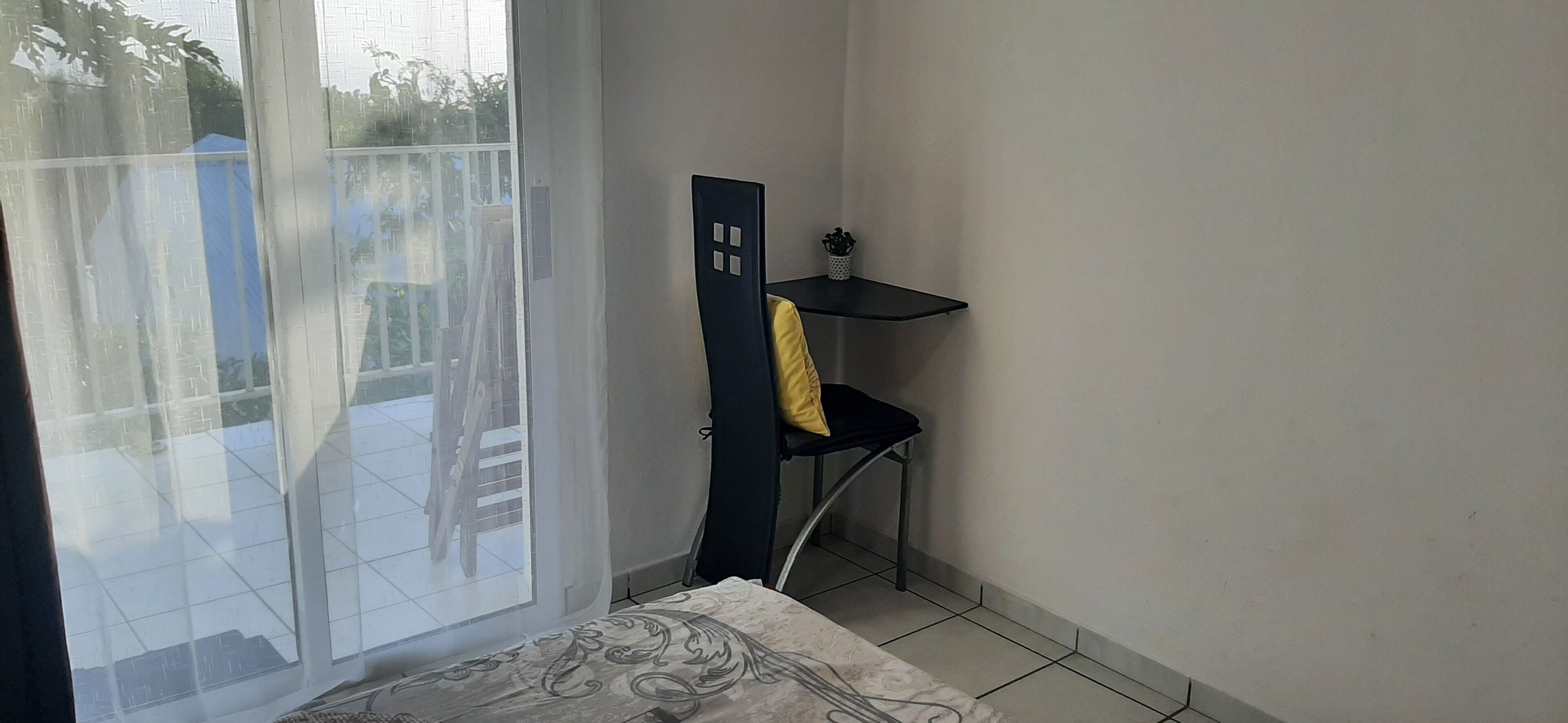 A room with a bed, a desk, and a chair. There is a window with a view of a blue tent outside.