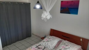 Un dormitorio con cama, cortina, lámpara de pared, un cuadro y un objeto blanco colgando del techo.