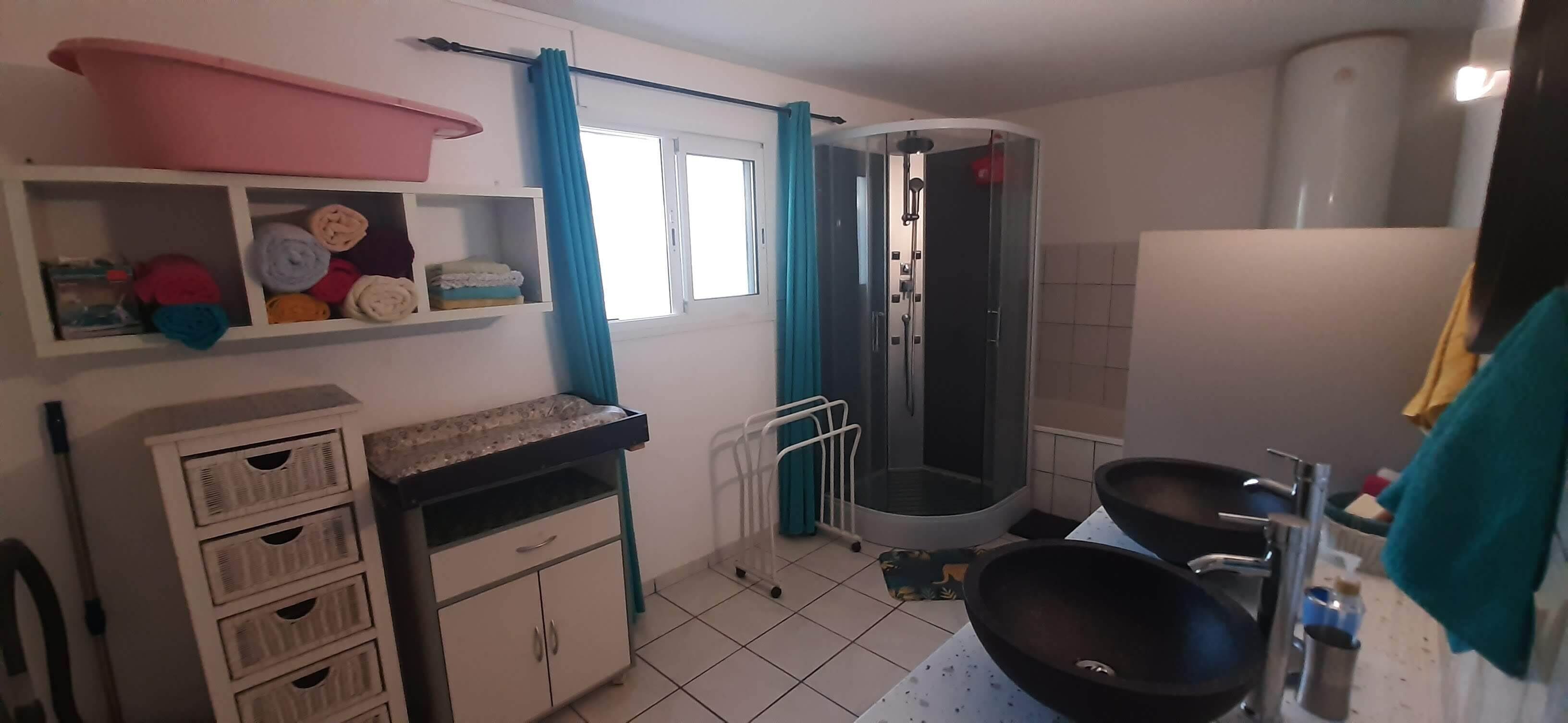 Een badkamer met douche, wastafel en opbergkastjes.