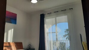 Una habitación con un ventanal grande, un ventilador de techo y un cuadro en la pared.