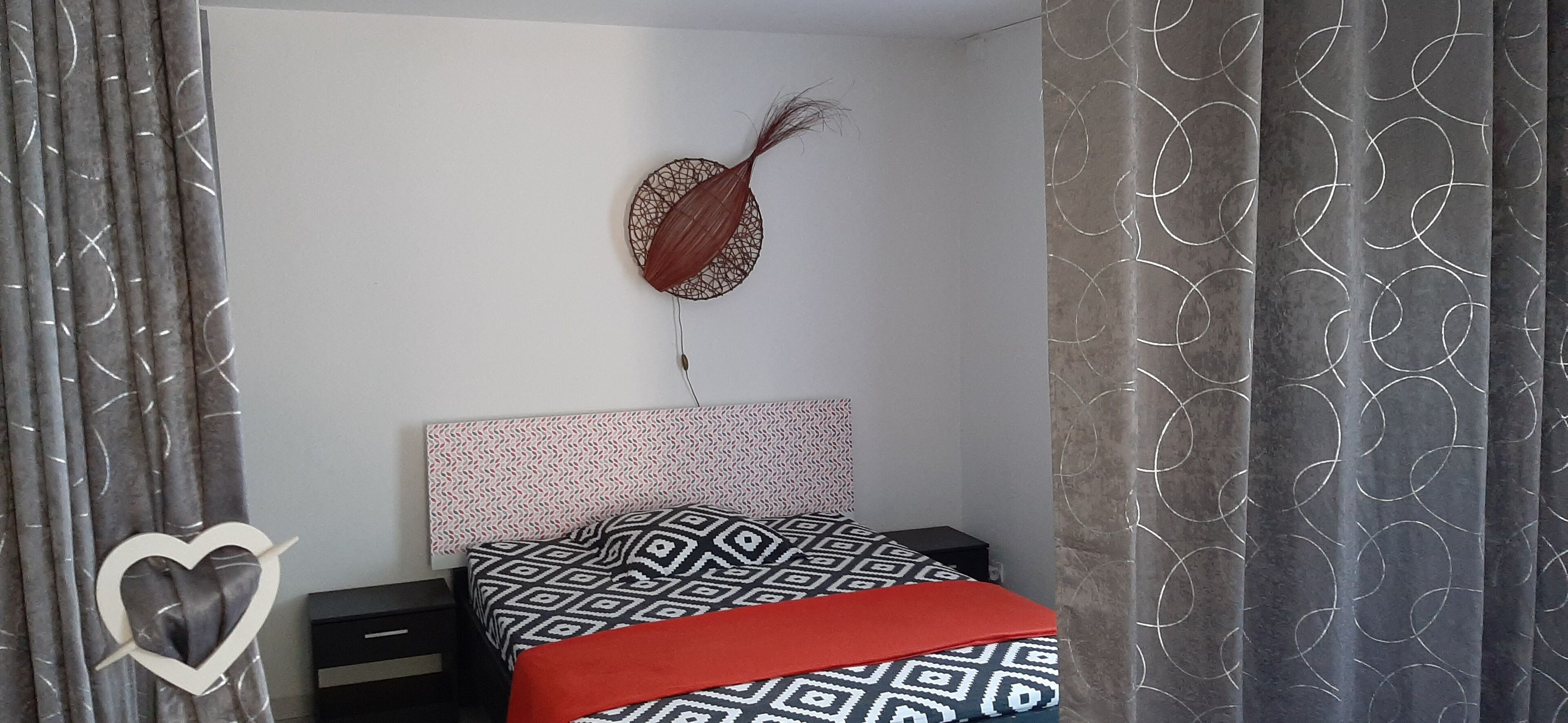 Une chambre à coucher avec une couvre-lit à motifs, une décoration murale et des rideaux ornés d’un motif circulaire.