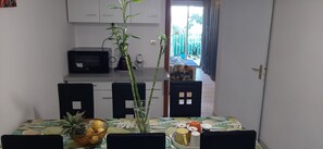 A dining area with a table set for four, a kitchen in the background, and a view of the outside. - PALMER : F3 Panoramic sea view 1-4 persons (Mont-Vert les Bas)