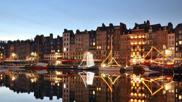 Un paysage urbain au bord de l’eau, avec des bâtiments historiques, un port tranquille et des structures illuminées.