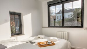 Une chambre d’hôtel avec deux lits, une fenêtre donnant sur une maison et un plateau avec des articles pour le petit-déjeuner.