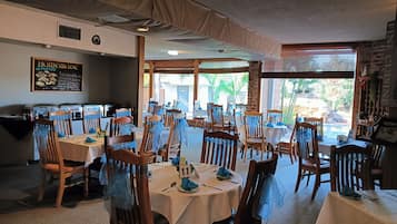 A restaurant with multiple tables and chairs, a chalkboard menu, and large windows.