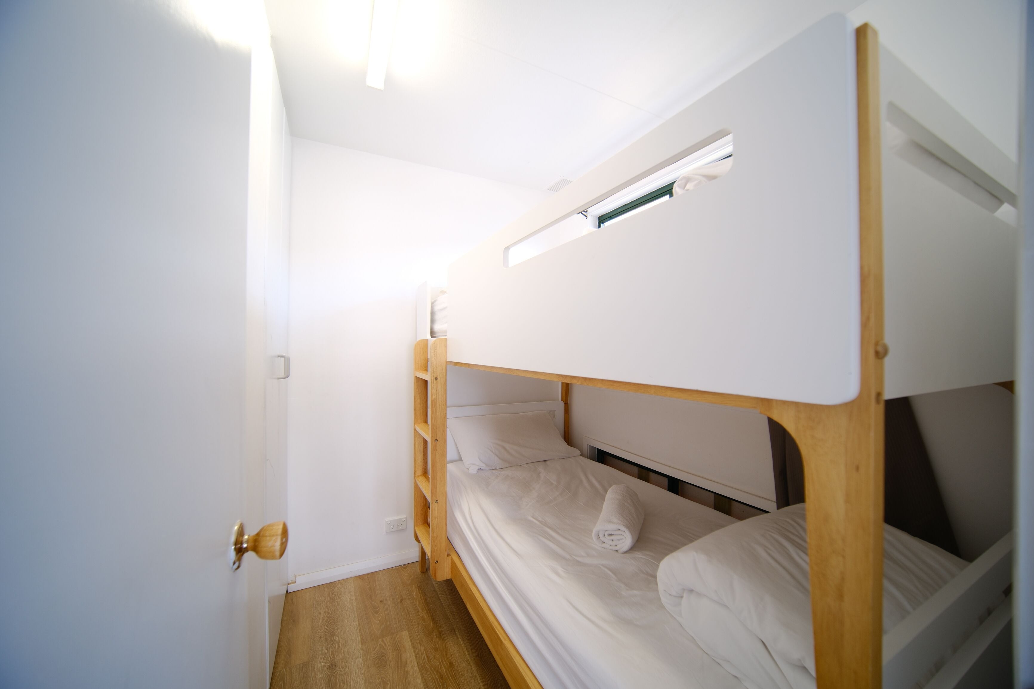 A bunk bed room with a wooden frame, white bedding, and a small window.