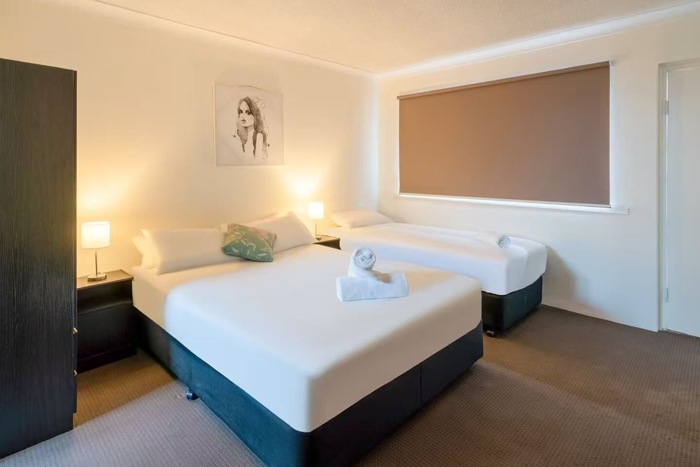 Habitación de hotel con una cama grande, dos mesitas de noche, una ventana y un cuadro en la pared.