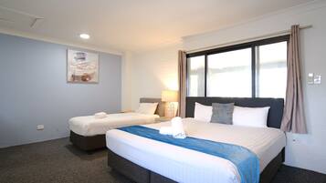 Quarto de hotel com duas camas, uma janela grande com cortinas, um quadro pendurado na parede e um abajur.