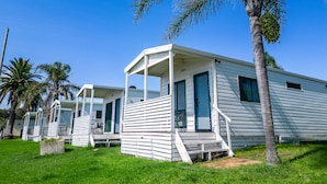A row of white mobile homes with a porch, surrounded by palm trees and grass. - Lakeside Inn Illawarra  (Windang)