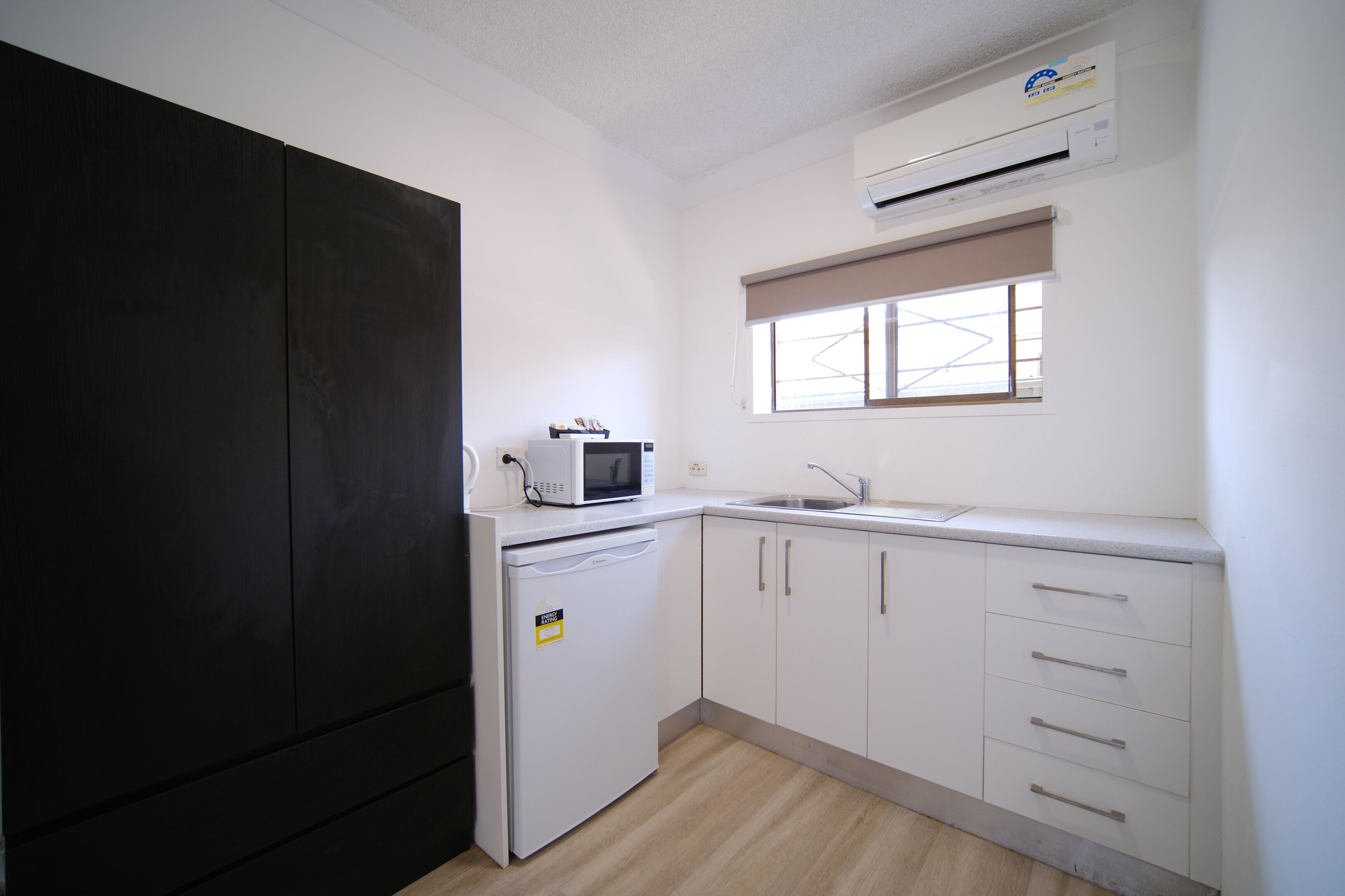 A compact kitchen with a microwave, a small refrigerator, a sink, and white cabinets.