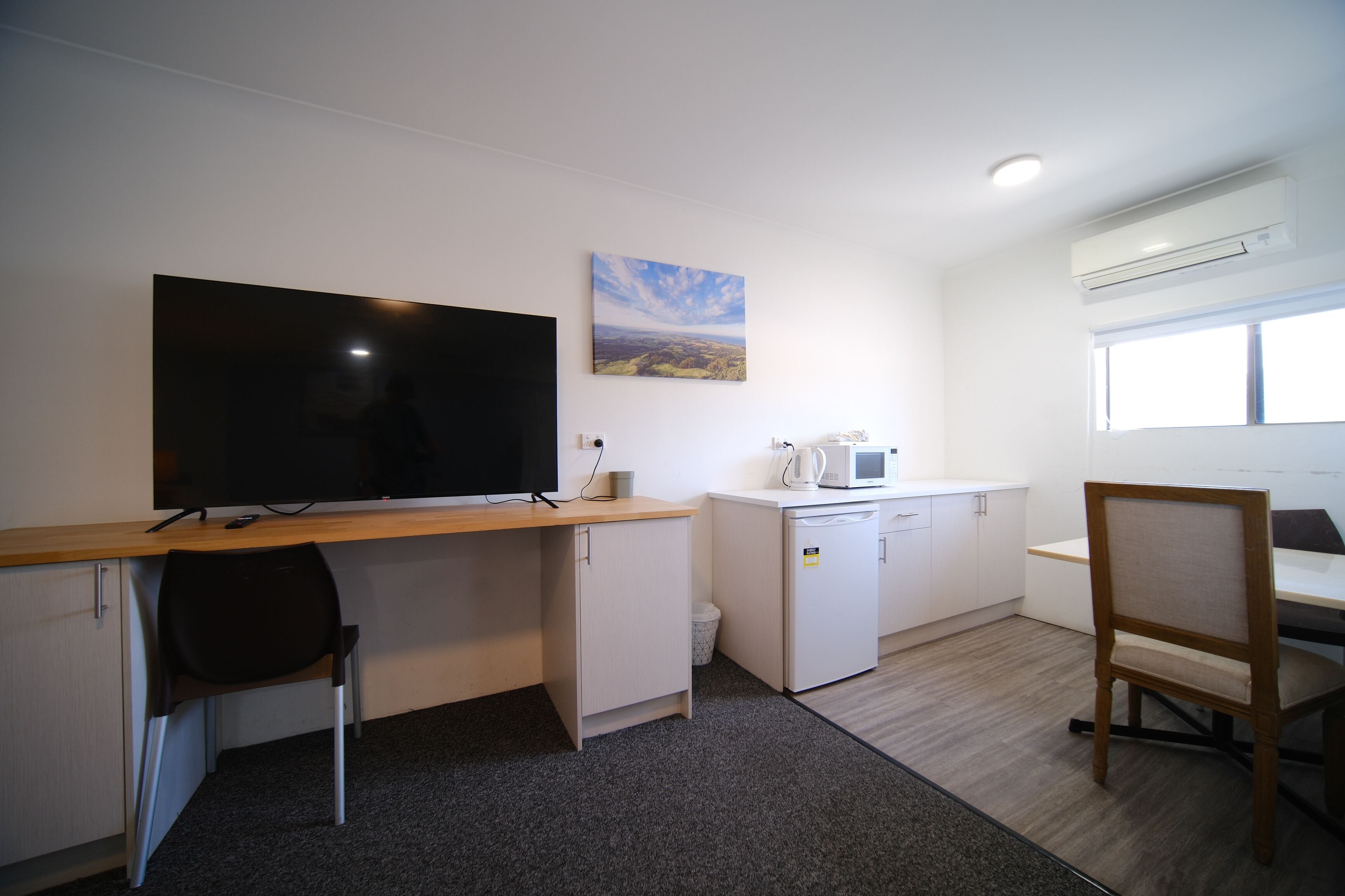 A compact kitchenette with a microwave, a small refrigerator, and a coffee maker. There is a large flat-screen TV mounted on the wall above a wooden desk.