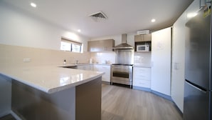 A modern kitchen with a central island, stainless steel appliances, and light wood flooring. - Lakeside Inn Illawarra  (Windang)