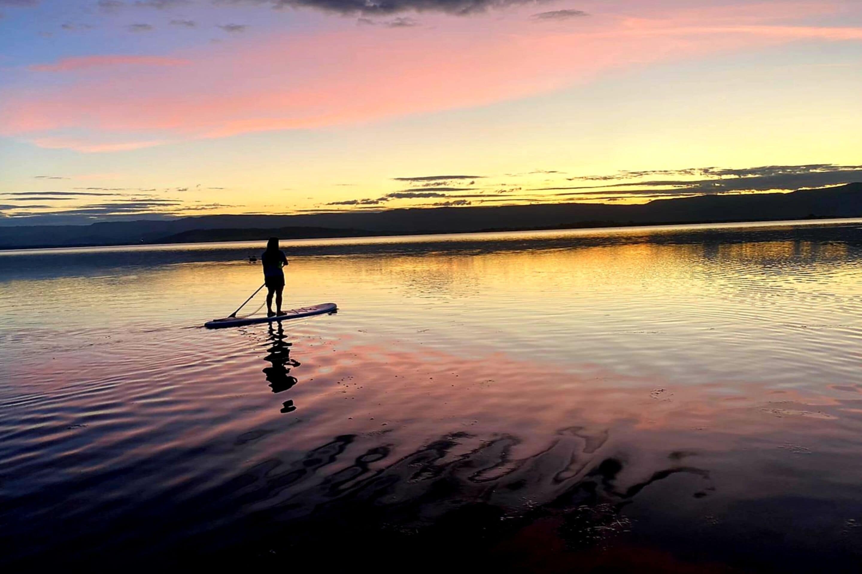 Una persona practica paddleboard en aguas tranquilas durante el atardecer.
