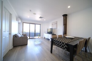 A modern living room with a sofa, a dining table with chairs, a TV, and a large window.