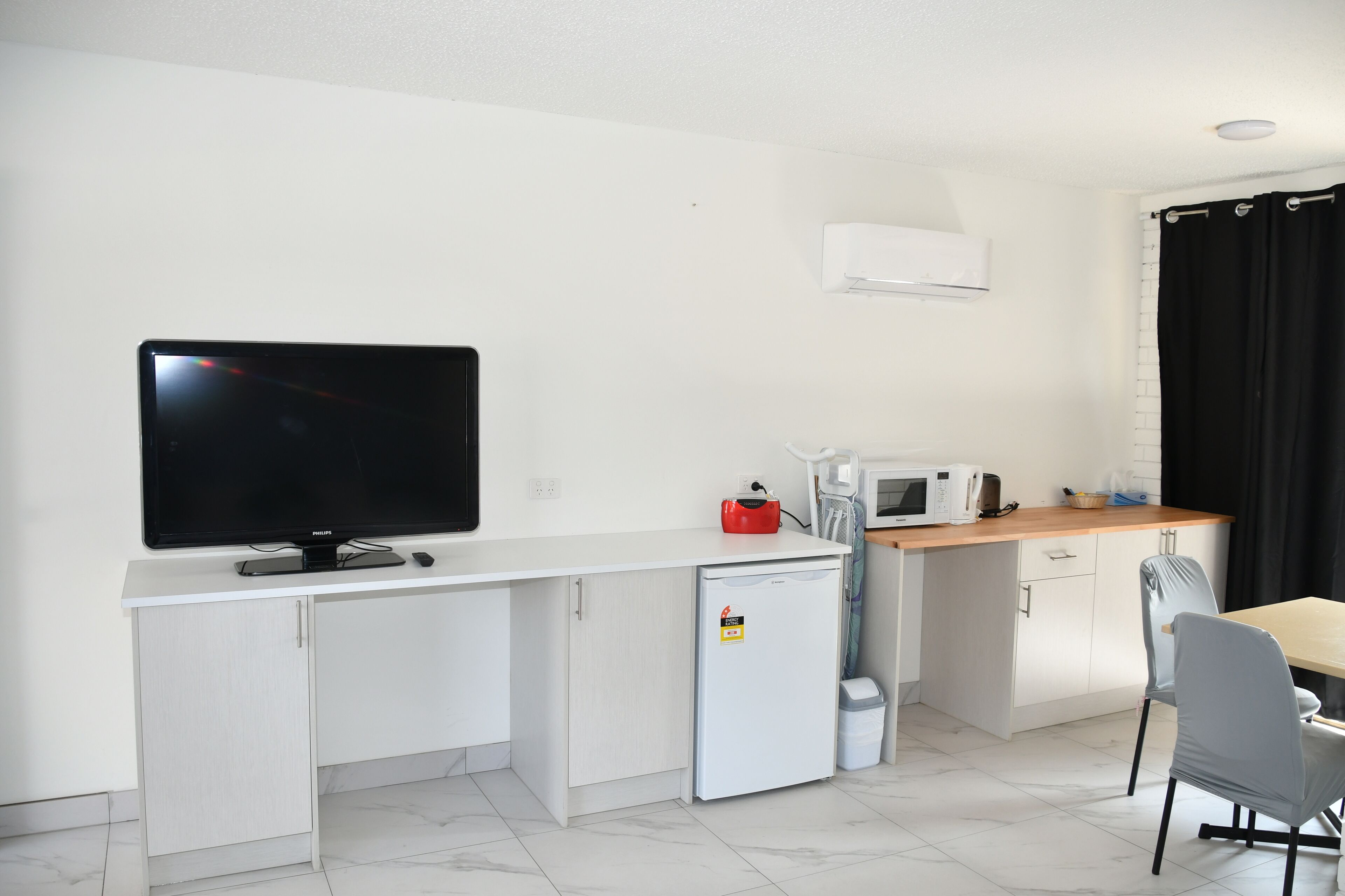 Een compacte kitchenette met een flatscreen televisie, een magnetron, een kleine koelkast en een houten aanrecht.