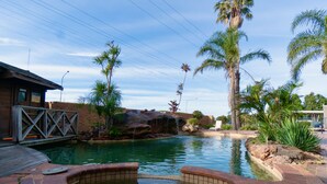 A swimming pool with a brick deck, palm trees, and a waterfall feature. - Lakeside Inn Illawarra  (Windang)