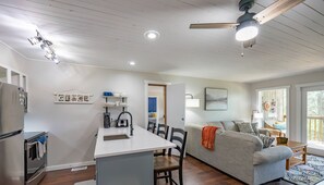 A modern kitchen with a central island, a dining area with a table and chairs, a gray sofa, and a ceiling fan.