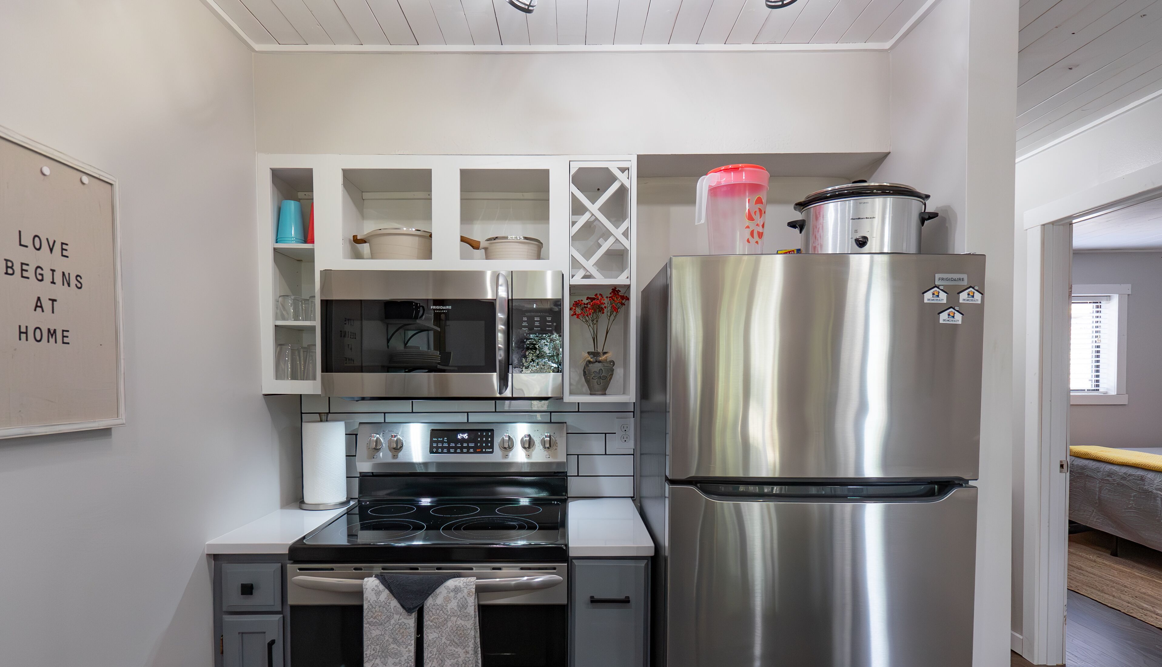 A modern kitchen with a stainless steel refrigerator, oven, and microwave. There is a white cabinet with glass doors and a wall-mounted sign.