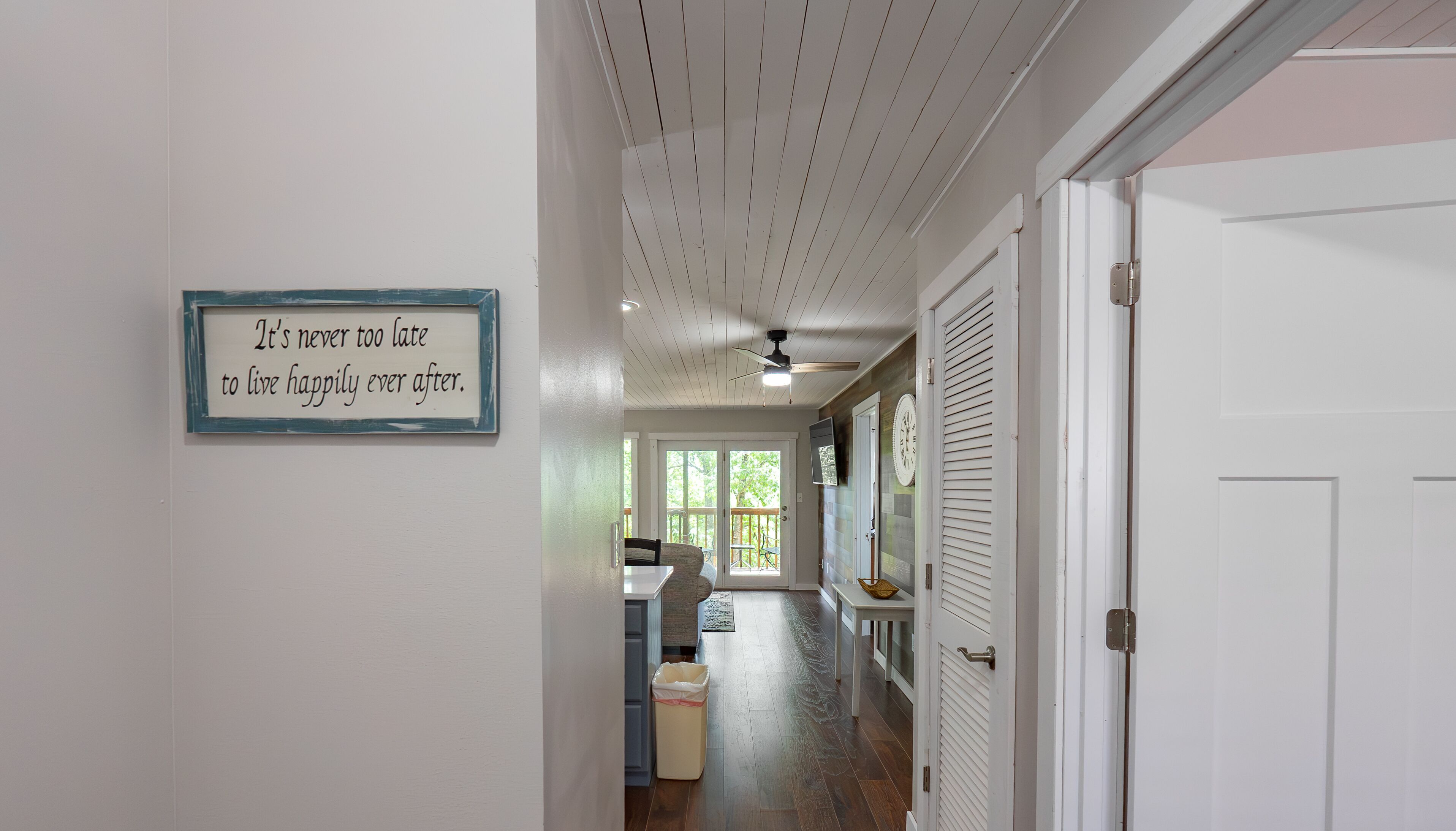 A hallway with a ceiling fan, a sign with a motivational quote, and a view of a deck area.