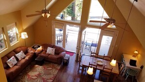 A loft-style living room with a brown leather sofa, patterned rug, and a dining area with wooden furniture. - Lake Almanor West - Lakefront Cabin (Chester)