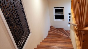 A wooden staircase with a red carpet at the bottom, a decorative metal grille on the left, and a small window with a white frame on the right. - Lake Almanor West - Lakefront Cabin (Chester)