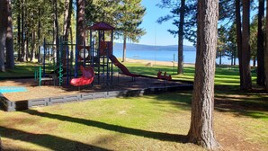 A playground with slides and climbing structures, surrounded by trees and a view of a lake. - Lake Almanor West - Lakefront Cabin (Chester)