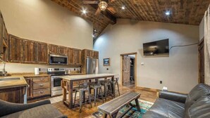A modern kitchen with wooden cabinets, a central island, and bar stools. - Your Basecamp to Glacier• Cozy 2BR w/ King + Queen (Coram)