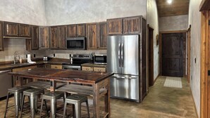 A kitchen with wooden cabinets, stainless steel appliances, and a central island with stools. - Your Basecamp to Glacier• Cozy 2BR w/ King + Queen (Coram)