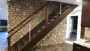 Una escalera con pared de piedra, barandilla metálica y zona de cocina con armarios y encimera.