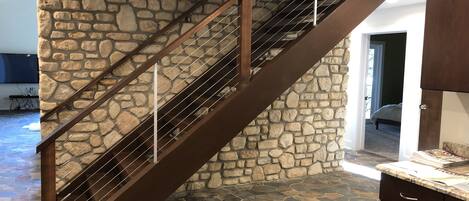 A staircase with a stone wall, a metal railing, and a kitchen area with cabinets and a countertop.