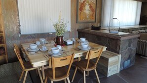 Un comedor con una mesa de madera preparada para cuatro personas, rodeado de paredes de piedra y un cuadro.