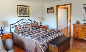Quarto com uma cama grande, penteadeira de madeira, duas mesas de cabeceira com luminárias e uma porta que dá para outro cômodo.