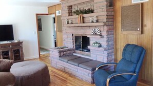 Una sala de estar con chimenea de piedra, un televisor sobre un mueble de madera y un sillón azul.
