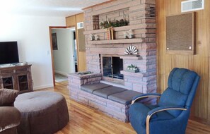 Relax by the fireplace in this inviting living room, featuring a comfortable armchair and TV on a wooden cabinet.