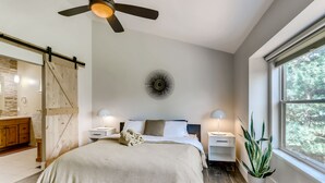 A bedroom with a bed, bedside tables, a ceiling fan, a wall-mounted light, a window with a view of trees, and a sliding barn door. - One of the nicest house rentals available in Lyons, Colorado (Lyons)