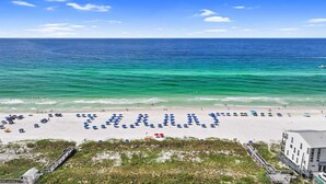 A beach with a clear view of the ocean, a sandy beach, and a building in the background. - Beach Retreat 407  Gulf Front, Dog friendly, Beach Service (Miramar Beach)