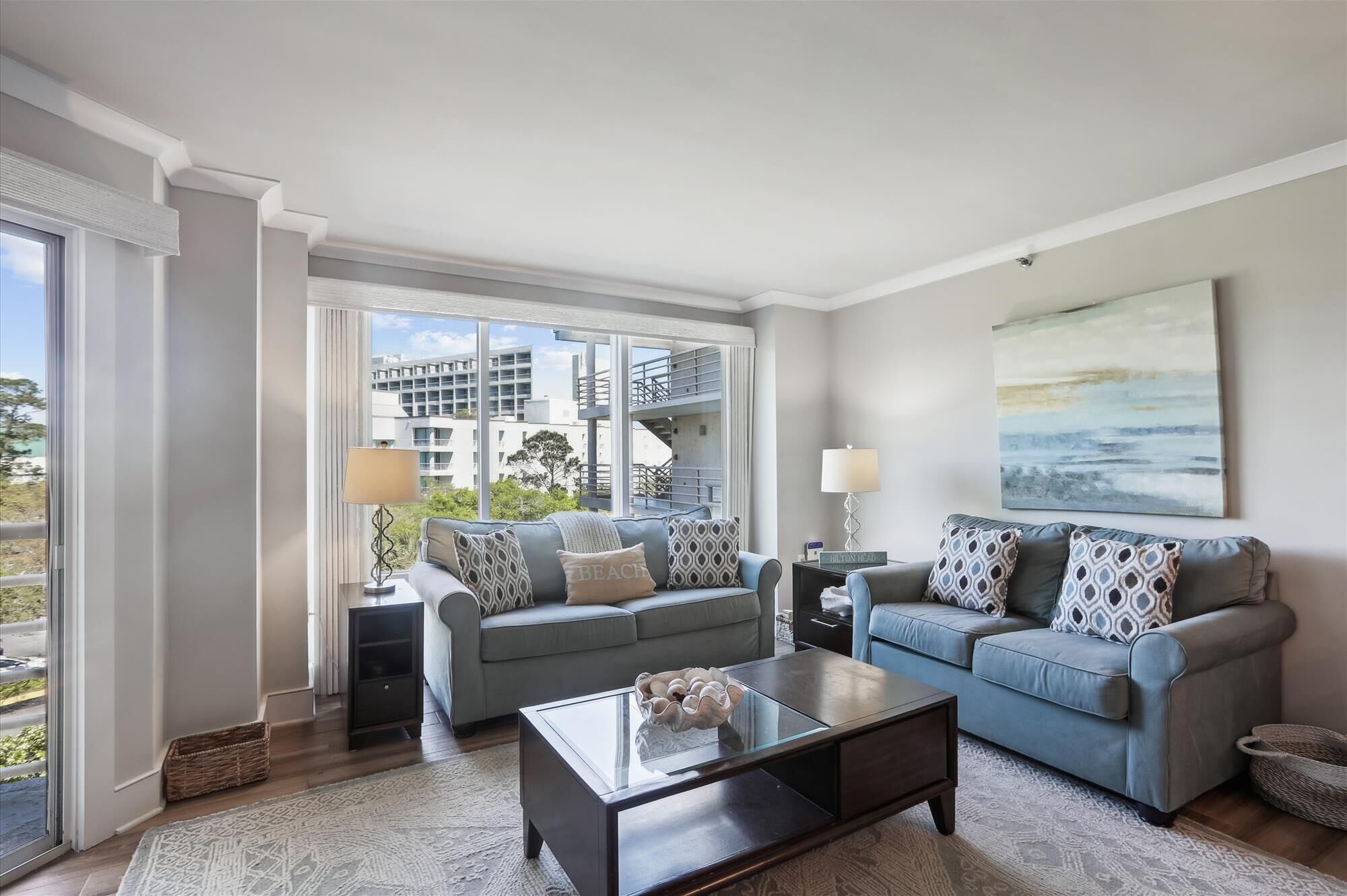 A modern living room with two sofas, a coffee table, and a large window offering a view of a building and greenery.