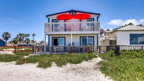 Un edificio frente al mar de dos pisos con un balcón y sombrillas rojas.